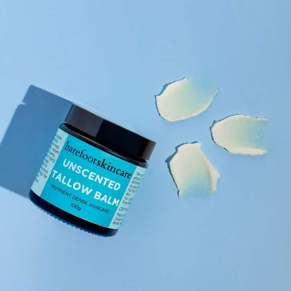 Barefoot Skincare Unscented Tallow Balm jar with scattered natural balm pieces on blue background